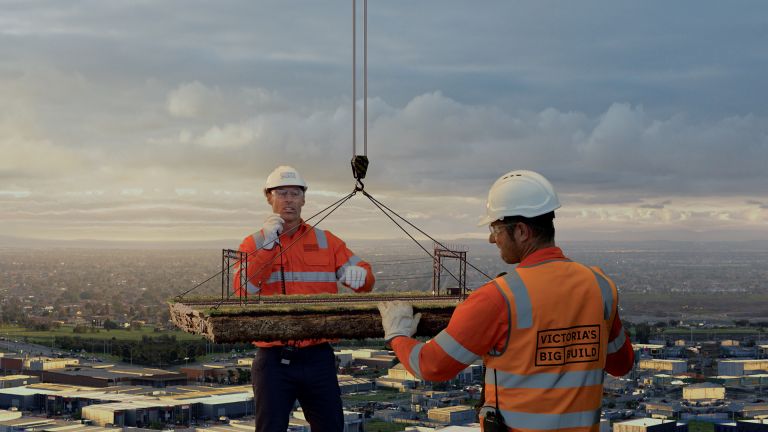 Two giant construction workers lift a section of rail line into place