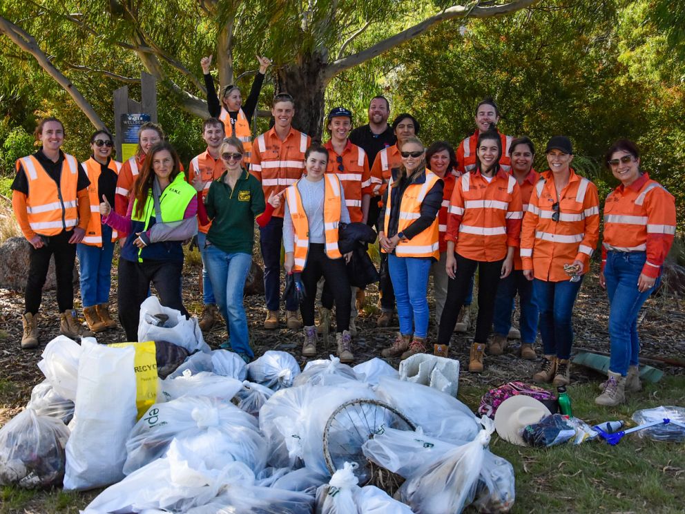 Large group of workers in hi-vis orange standing behind bags of rubbish collected.