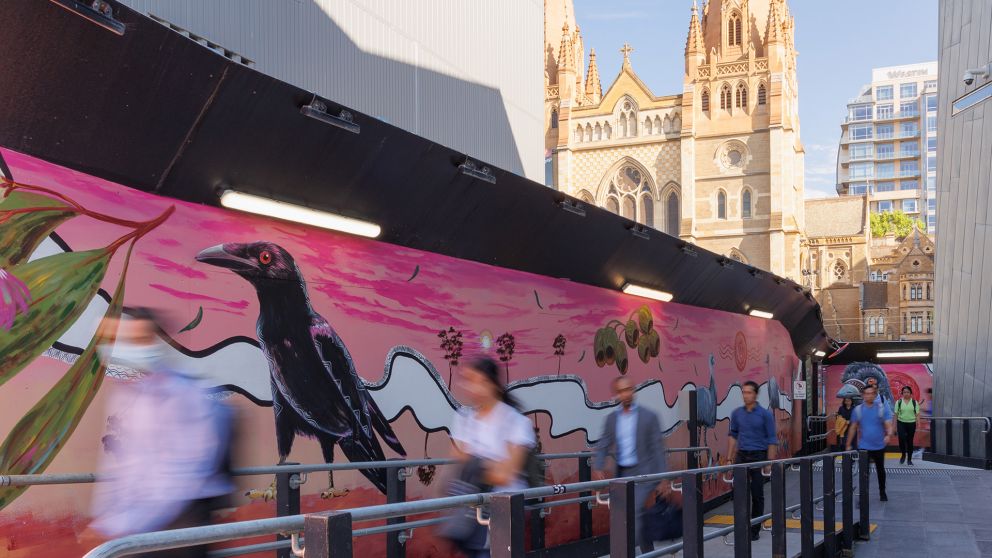 A crow and other birds are painted on a wall next to a pedestrian walkway