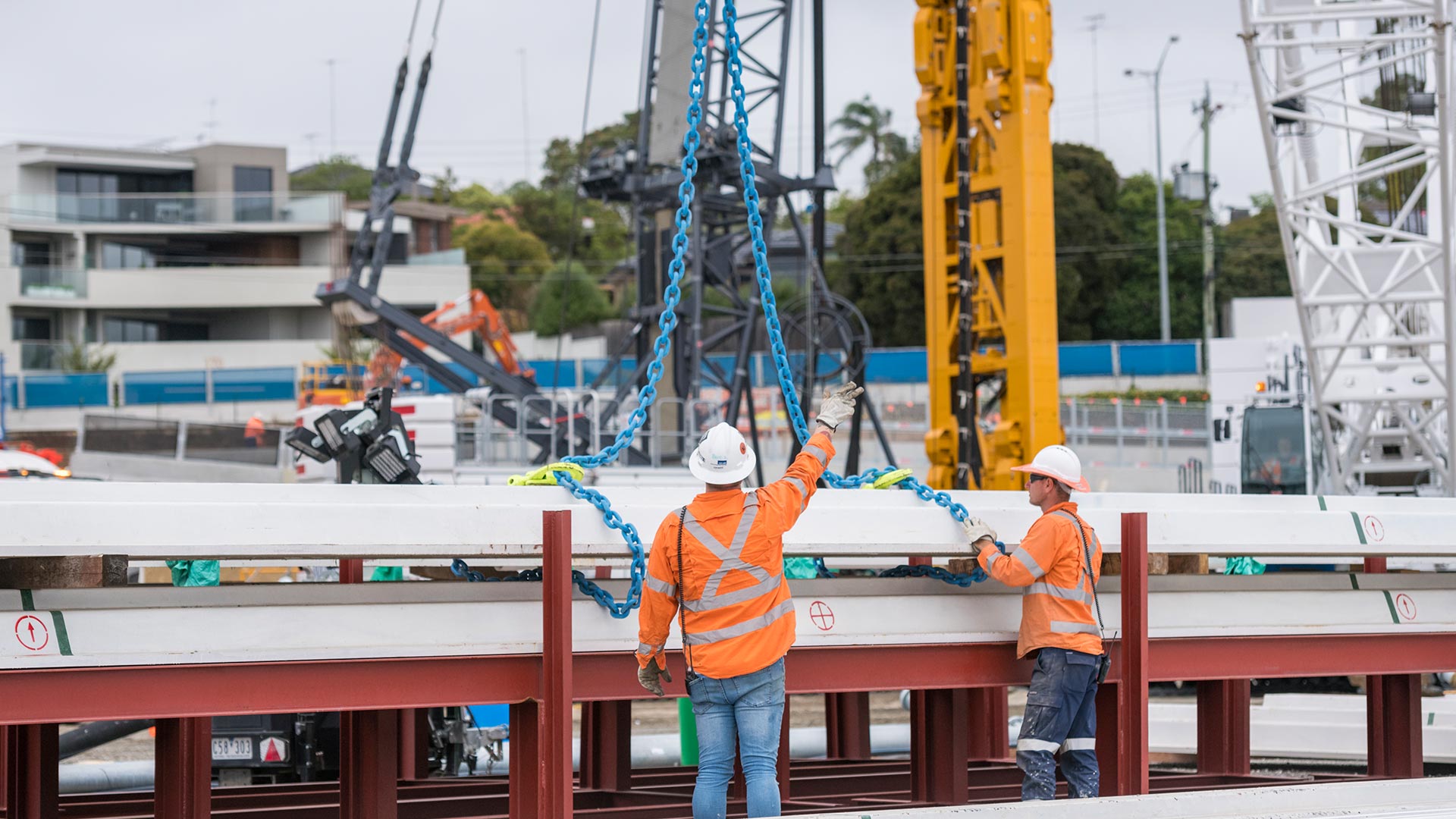 Two construction workers in high vis and protective clothing checking a load and guiding the crane operator.