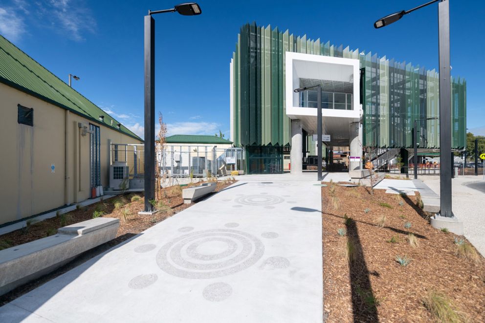 An image of a path with sandblasting and landscaping in surrounds, with a large building at the rear