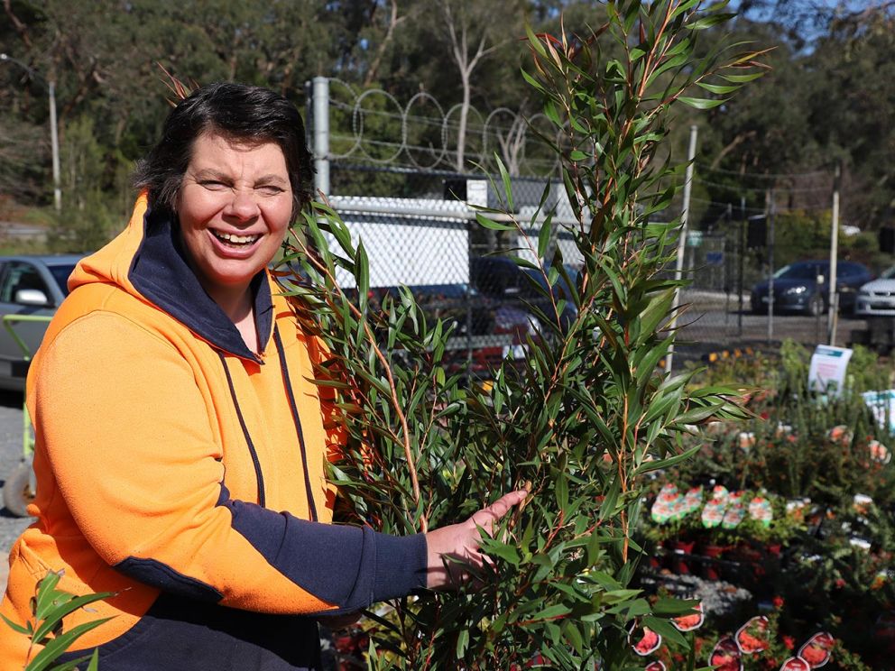 A gardener holding a native tree and smiling.