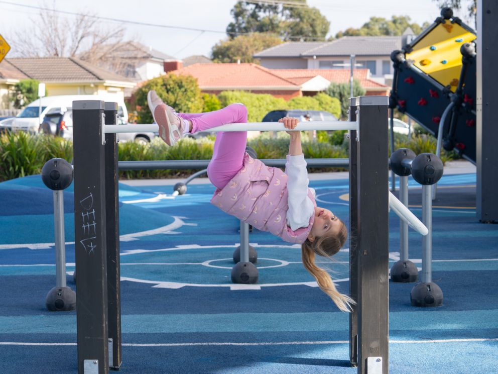 Kid hanging upside down on Clayton playground equipment