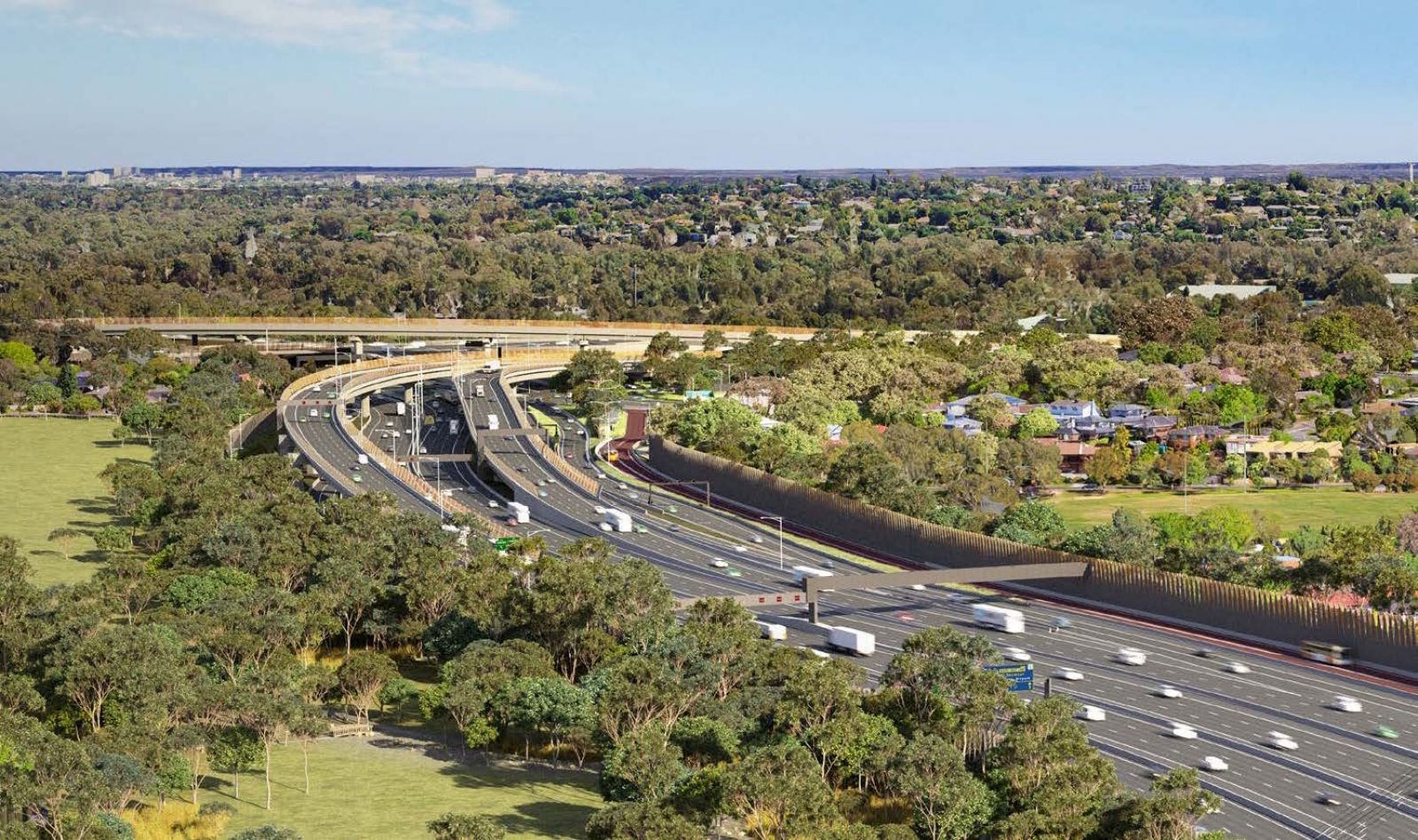 Aerial view of a multi-lane highway with surrounding greenery and suburban areas. The road curves and includes multiple lanes, ramps, and overpasses, bordered by sound barriers and trees.