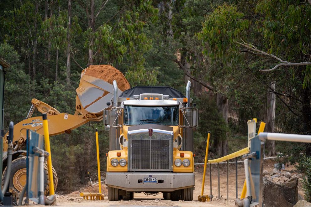 A yellow truck waits as an excavator loads it with material