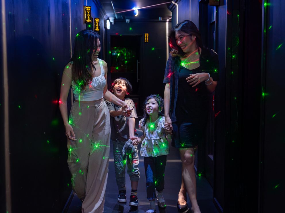 A family of four walking through a hallway lit with neon lights and lasers.