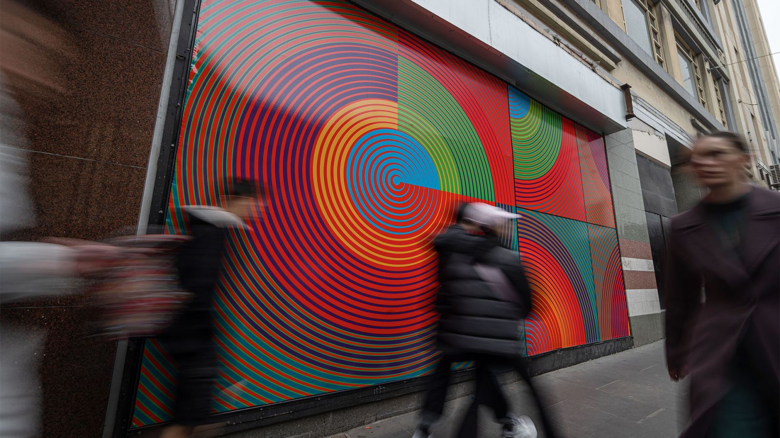 Figures walk past a colourful artwork on a hoarding 