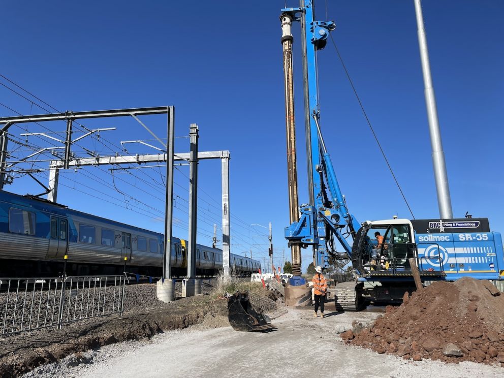 A train passes by the piling rig on the western side of the rail line at Old Calder Highway