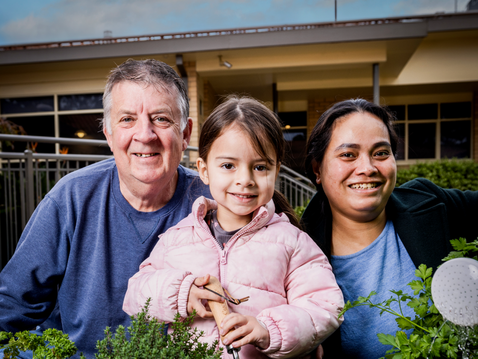 Image shows family of 3 smiling in the garden.