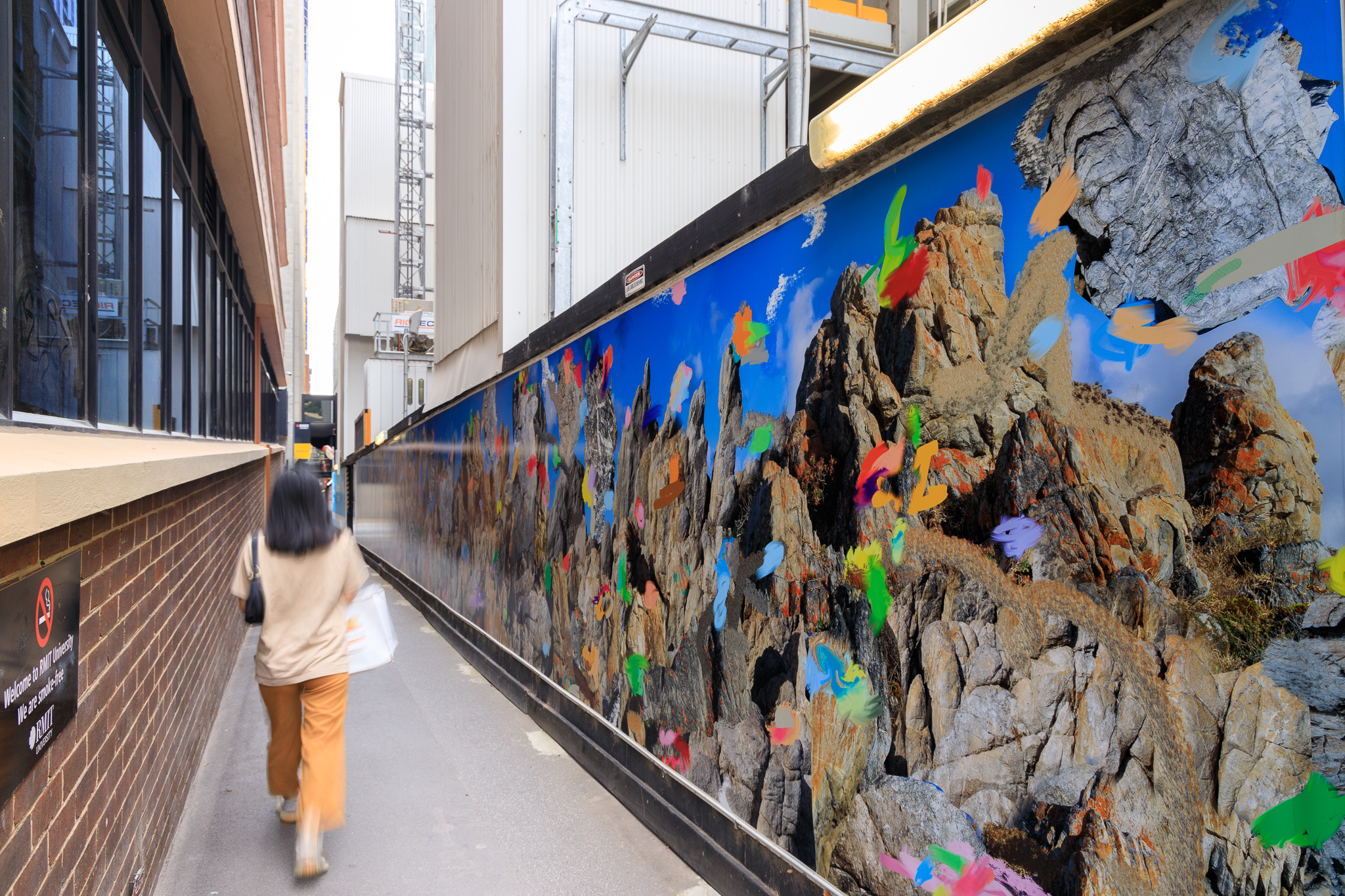 A woman walks past a photographic mural featuring big rocks and coloured flecks