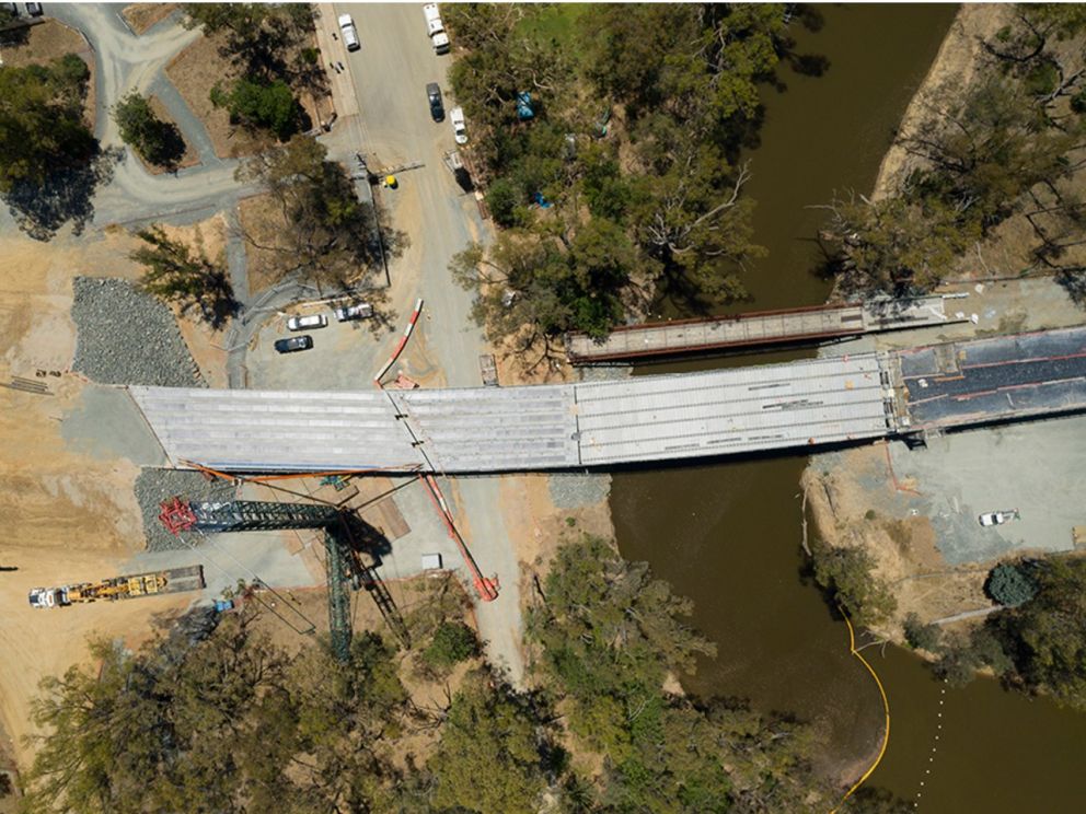 Birds eye image of the last beam and separate steel truss being installed over the river