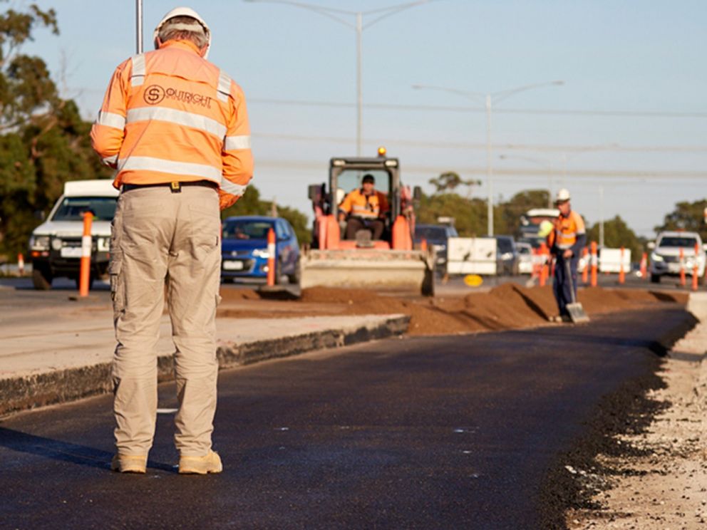 Image of a construction worker marking the road and moving earth in the background