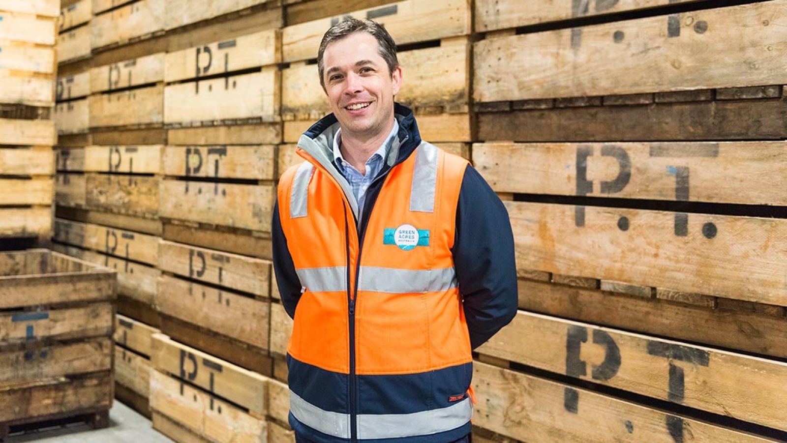 A person wearing an orange high-vis vest standing in front of stacked pallets.