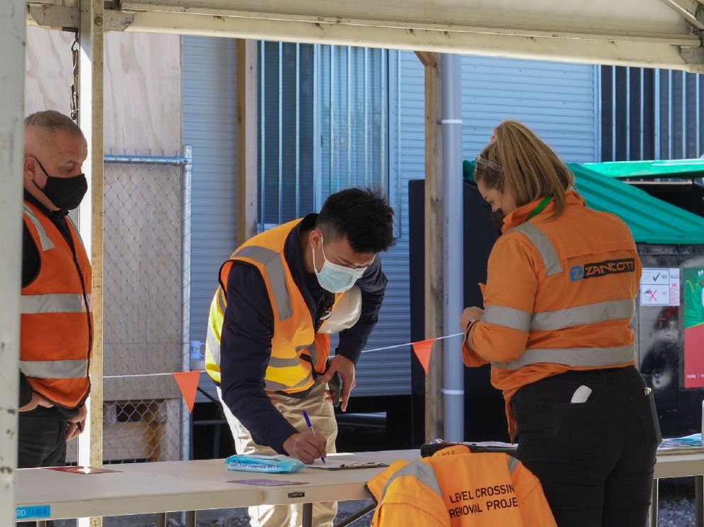 Woman behind a desk checking in 2 males at entrance of site.