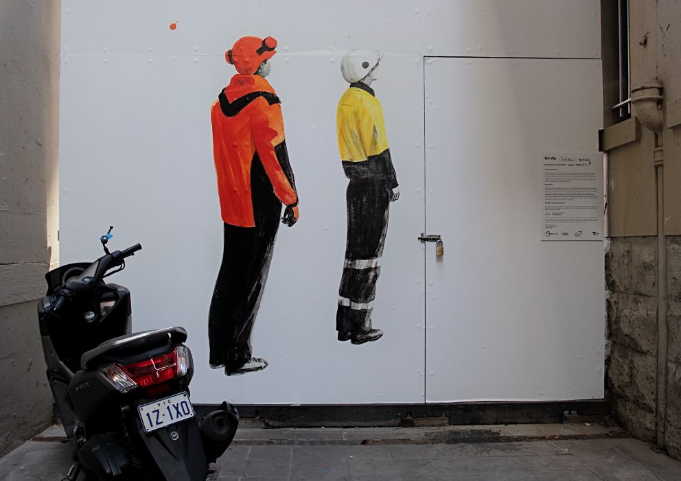 An artwork of two people standing looking upwards, on a temporary wall at the end of a laneway