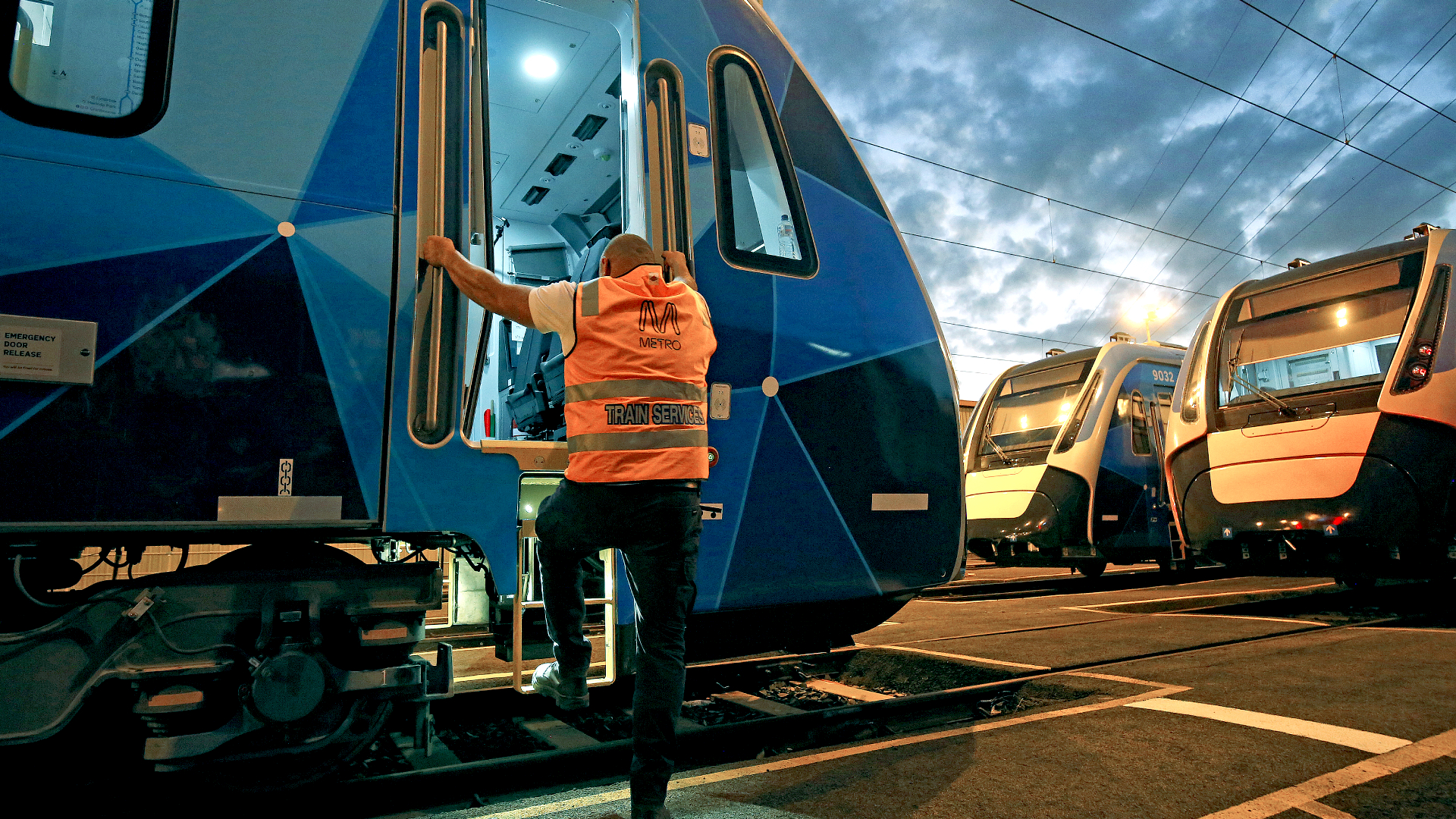 A worker in a high-vis orange vest stepping into the front cabin of a Metro train