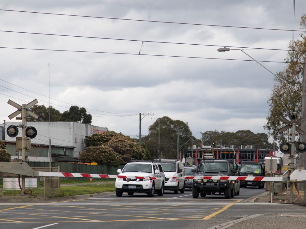 Traffic waiting at the Greens Road level crossing as a train passes through.