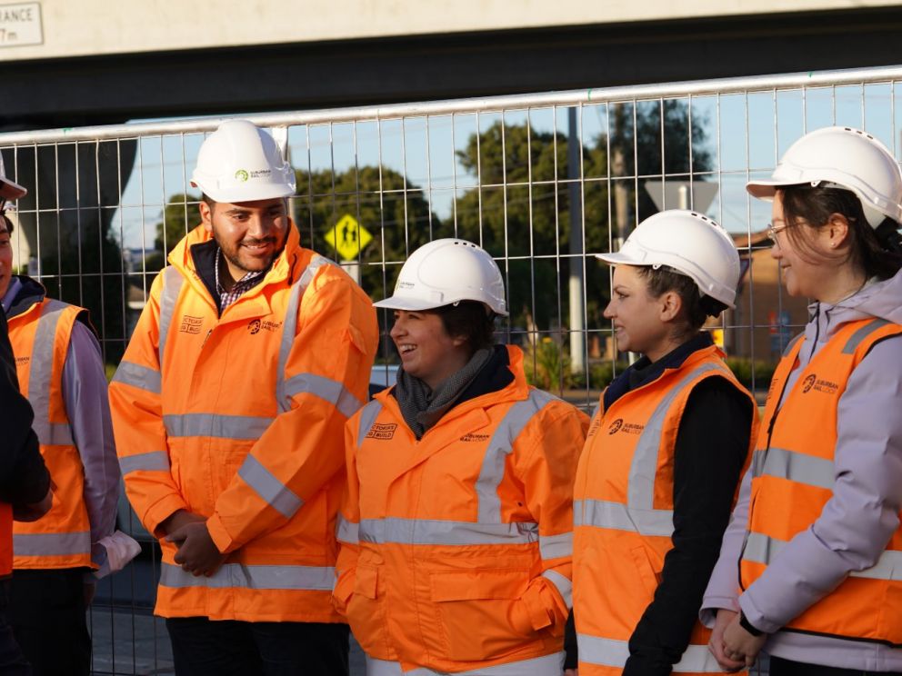 Five graduates standing at construction site in high-vis jackets and safety helmets