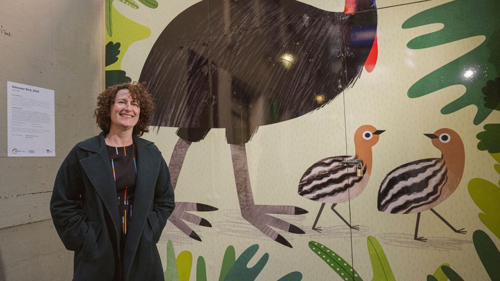 Artist Sarah Allen stands in front of her Dinosaur Bird artwork in Scott Alley