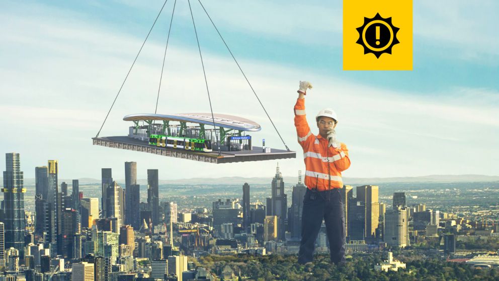 A giant-sized man in a hard hat and work wear stands to the south of the Melbourne CBD, helping to manoeuvre a tram stop and underground station entrance, which is suspended from a crane. 