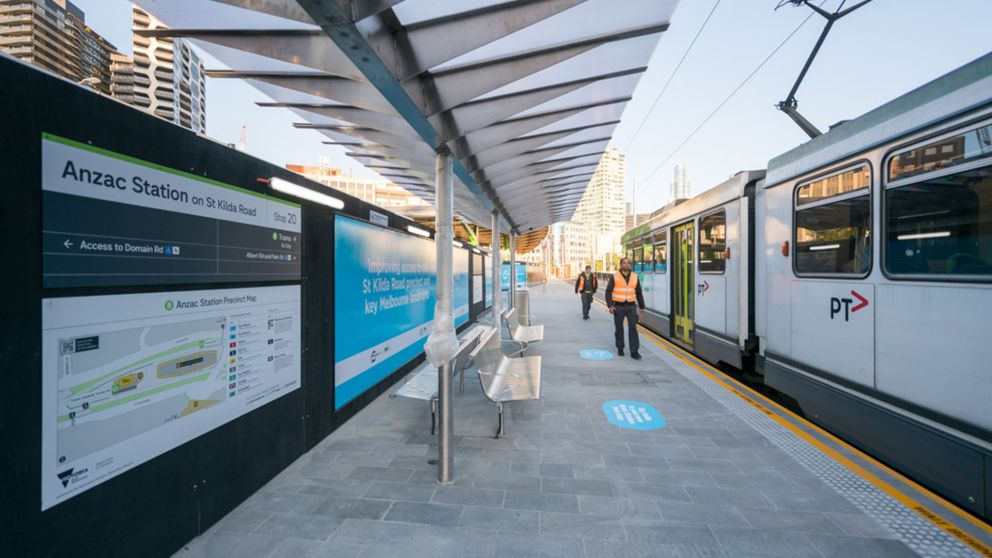 A tram is stopped next to a passenger platform and hoarding