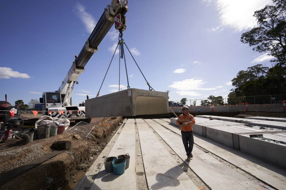 A spotter safely guiding a culvert onto a base slab on Hall Road