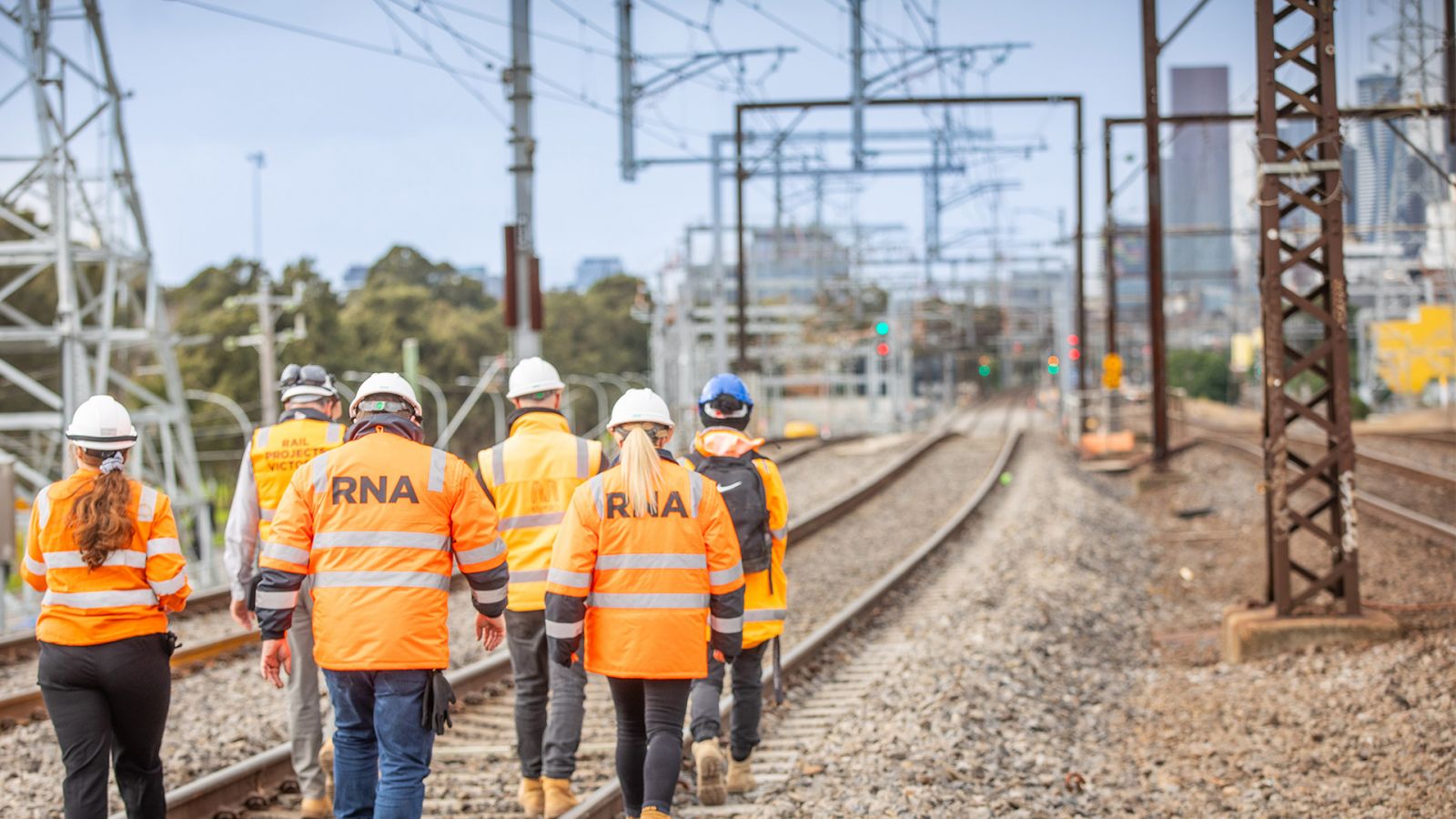 6 workers with their backs to the camera, walking towards the city skyline along the Sunbury Line