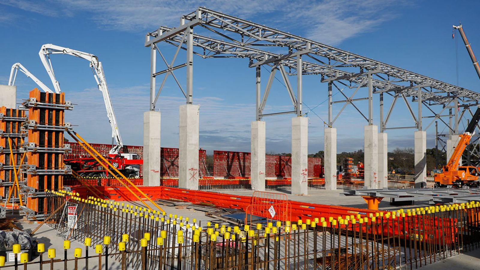 A North East Link construction site where an enclosed conveyor belt is getting built. There are concrete pillars with a metal frame and a crane.