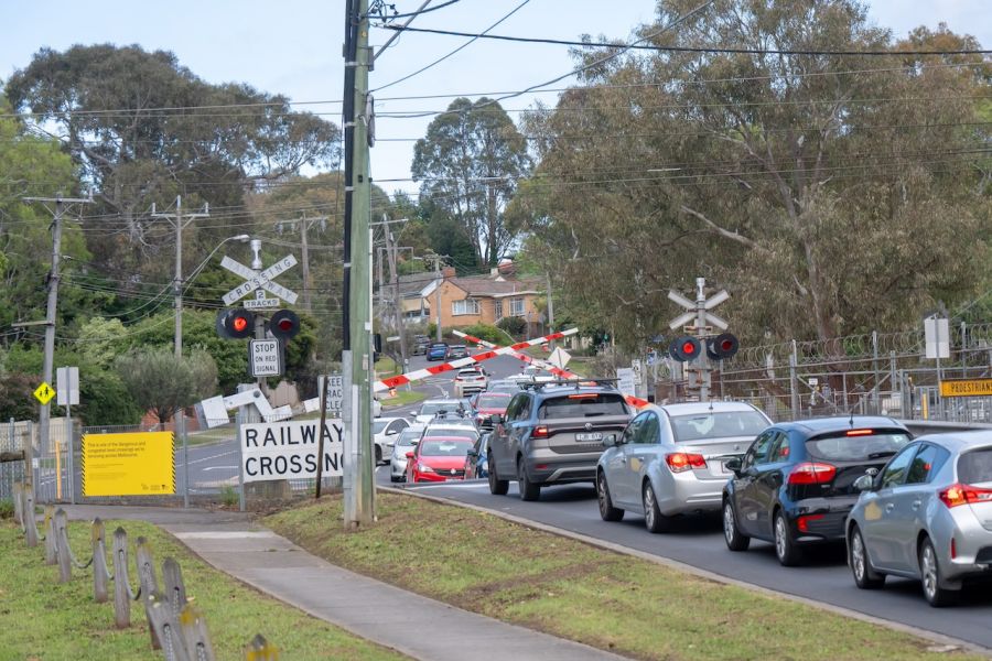 Boom gates down at Ruthven Street level crossing with a long line of cars stopped at the crossing