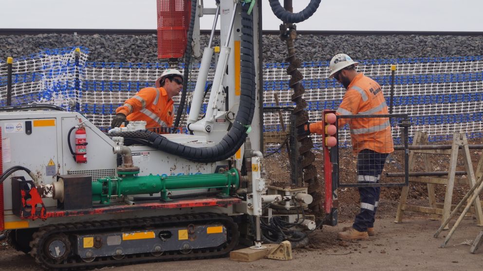 Two workers in orange hi vis working with a piling rig