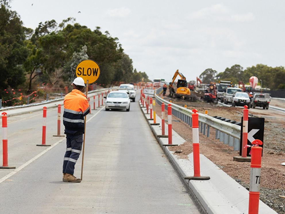 An image of a traffic controller stopping traffic due to roadworks.. Can see construction occurring in the background