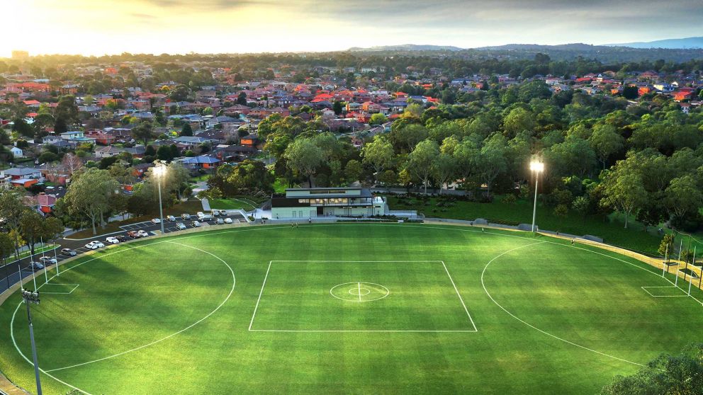 Aerial artist impression of Binnak Park oval at dusk. The new pavilion and car park is shown at one end of the oval and floodlights are turned on and the oval is surrounded by trees and houses. 
