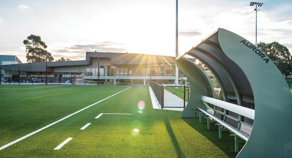 The sun setting on Greensborough College oval looking towards the newly built pavilion. There's a small, covered grandstand in the foreground overlooking the new synthetic turf soccer pitch.