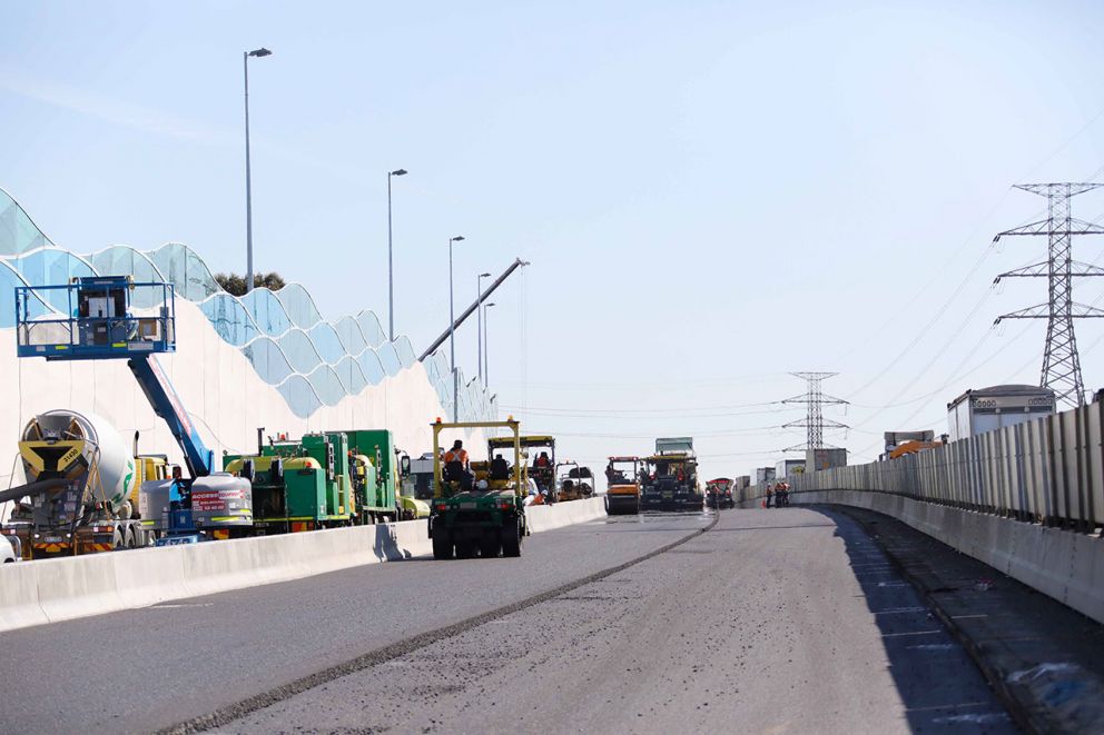 Photo of installed noise wall with crews working on asphalting road nearby