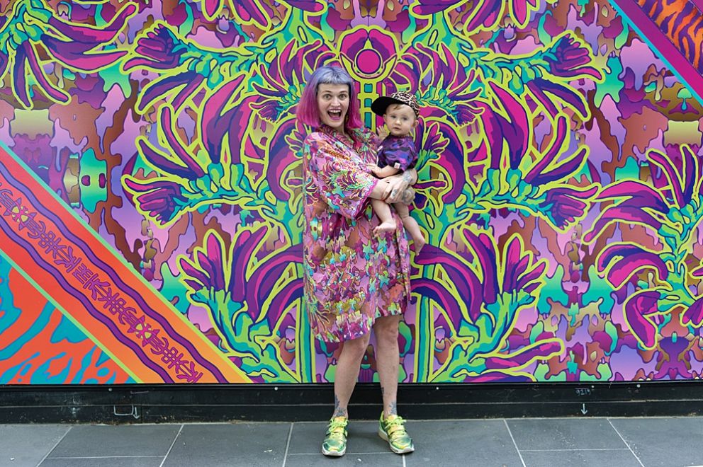 Nixi Killick with her child, excited posing in front of artwork. 