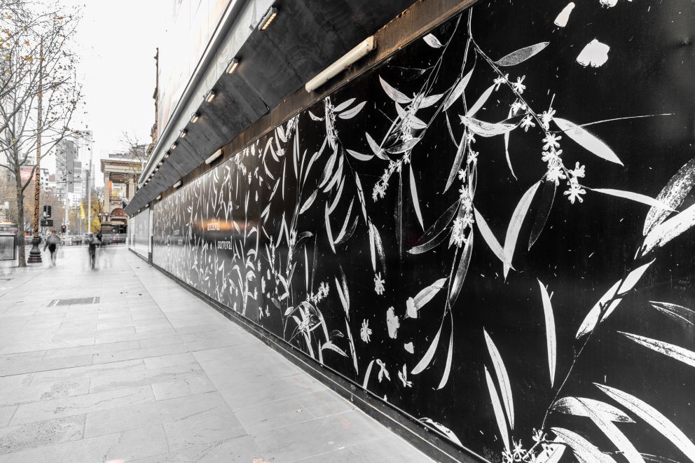 Artwork on construction hoarding in a street, black background with white leaves