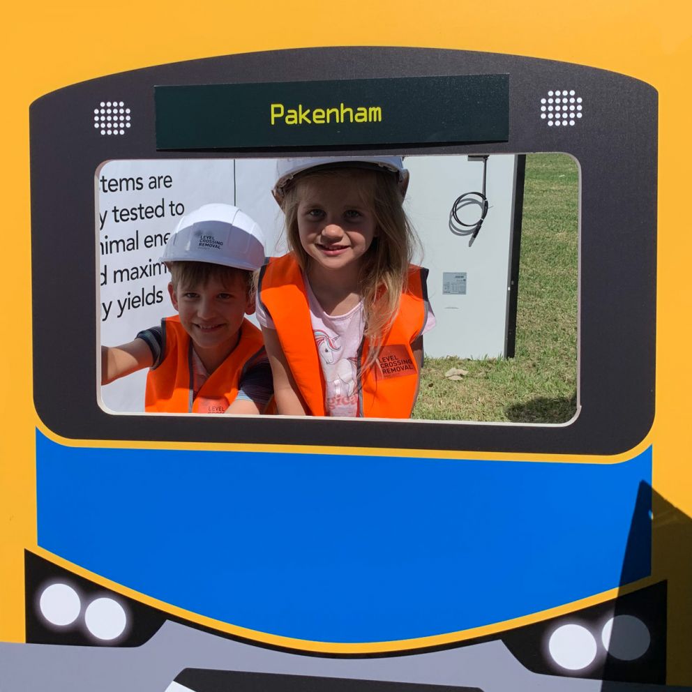 Two children standing behind a Pakenham train cut out.
