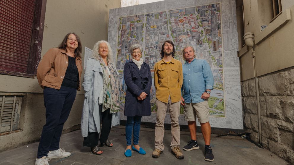 Five adults stand in front of the Melbourne Map artwork, smiling at the camera