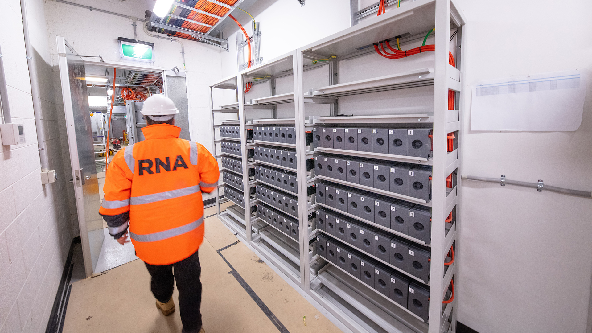 Person walking through servers area underground with RNA on the back of their high vis 