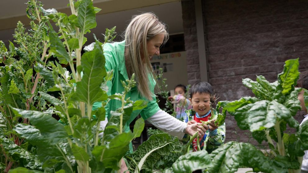 A teacher and preschool student in a vegetable patch smiling.