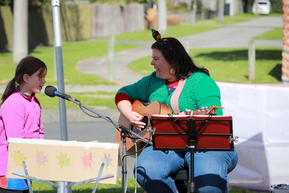 Woman sitting and playing guitar next to a young child singing