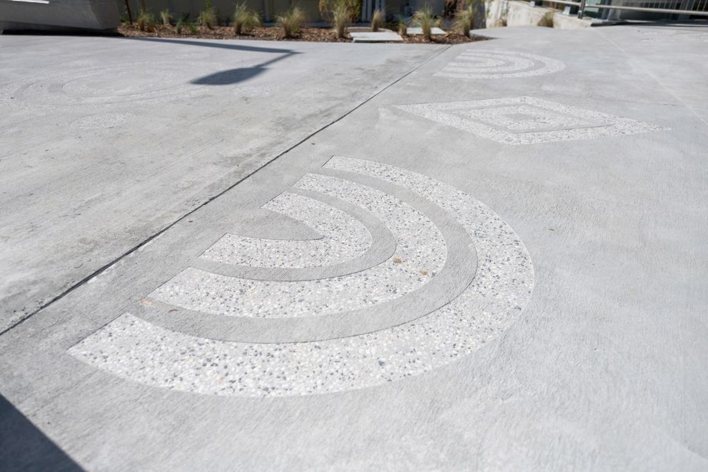 An image of sandblasted artworks in the ground of various shapes, with small landscaping plants in the background