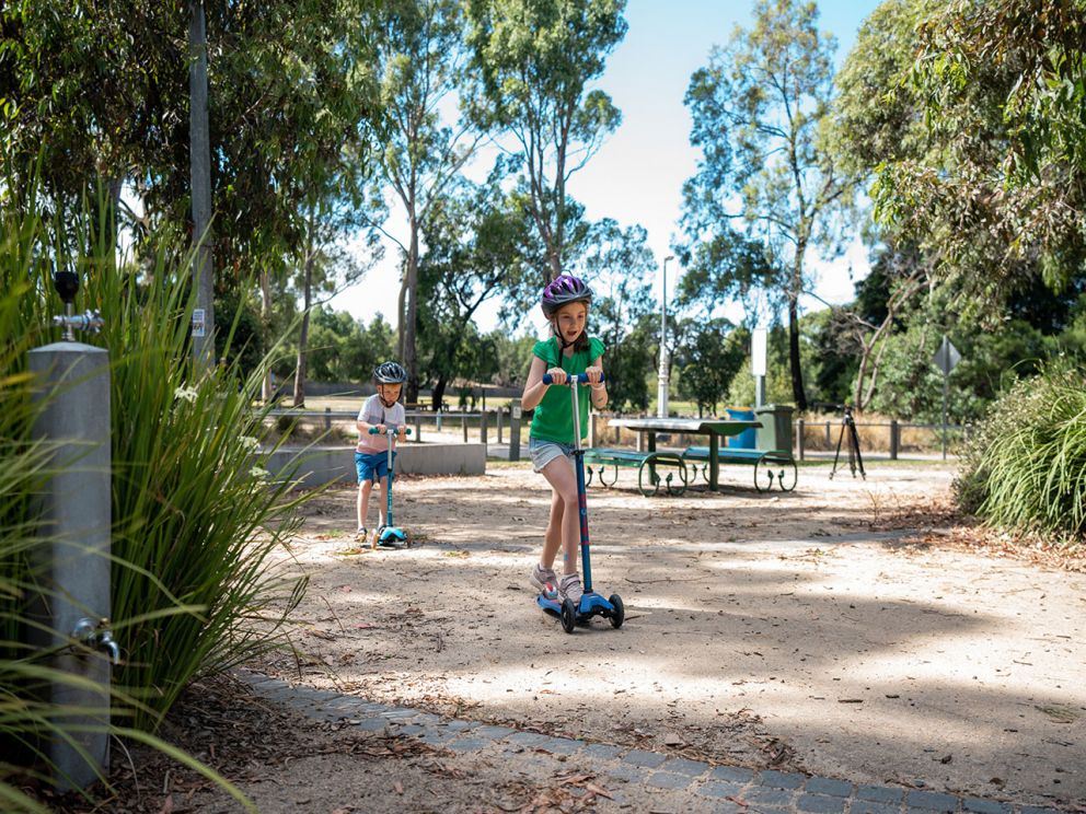 Two children on scooters riding through the Cheltenham picnic area