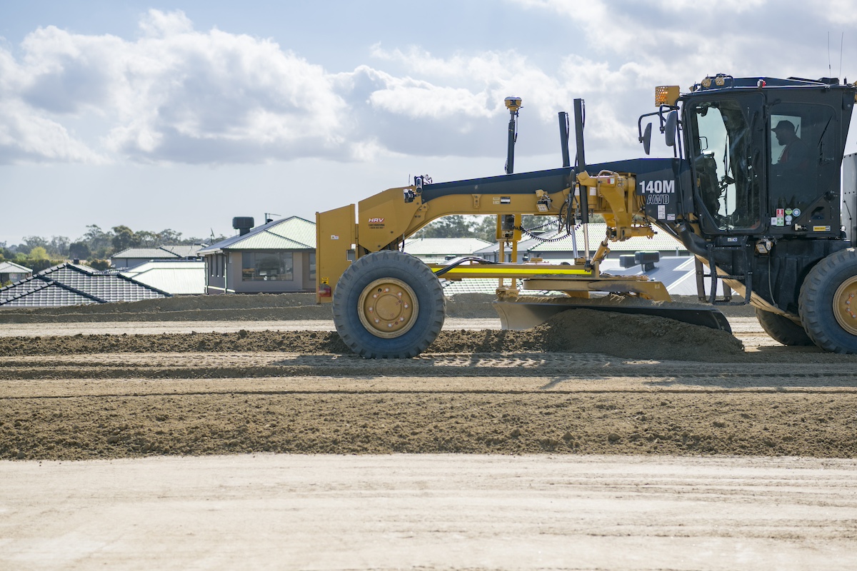 A grader smoothing out soil and material on site to form the foundations of the road bridge