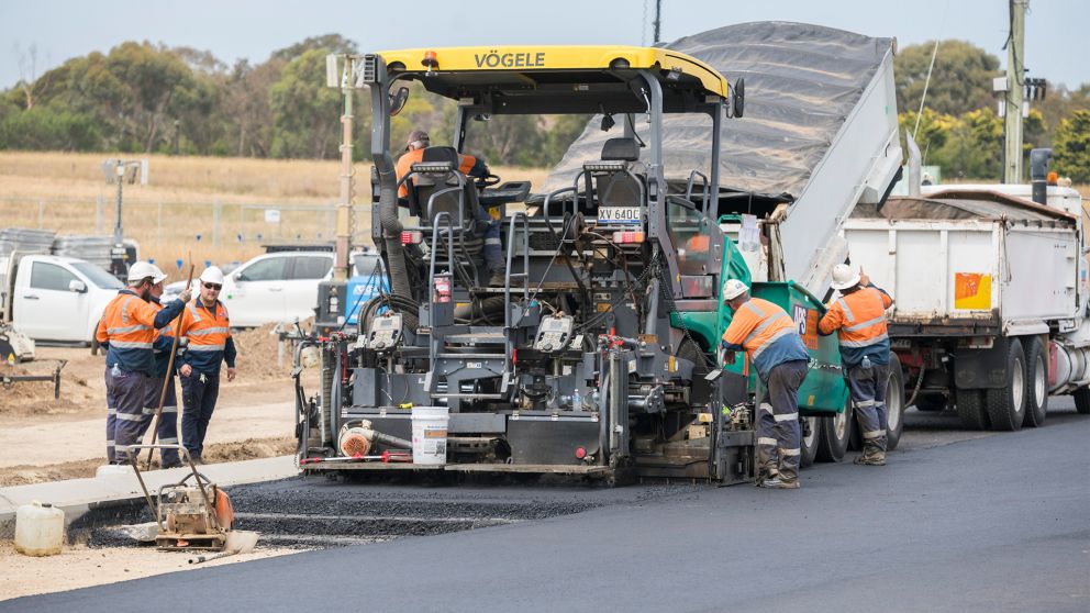 Team of workers standing alongside machinery asphalting the road on Surf Coast Highway/ 