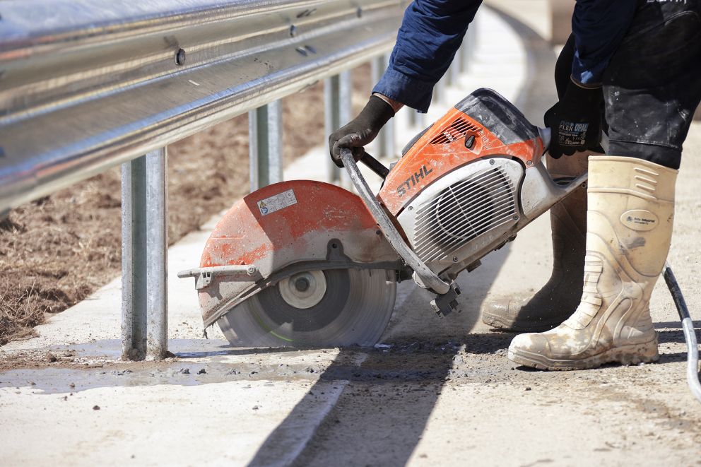 A crew member saw cutting joints in the concrete base under the guardrail.