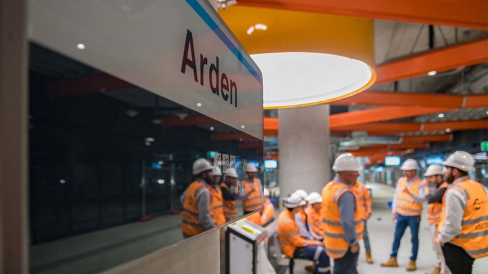 Workers in hi-vis gathered near Arden Station sign 