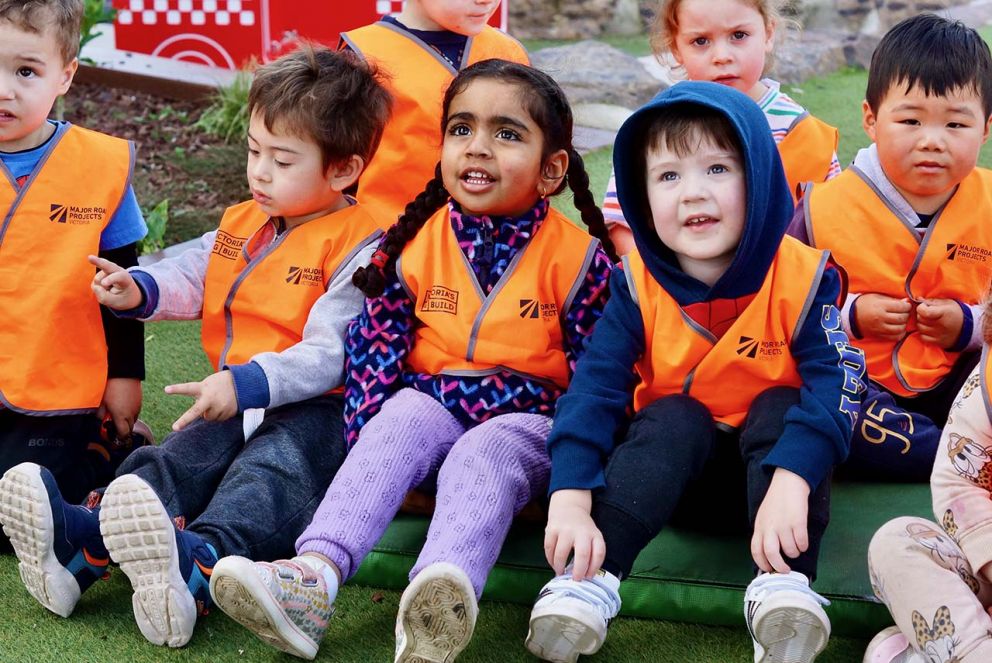 3 children sitting on the ground with high-vis vests on