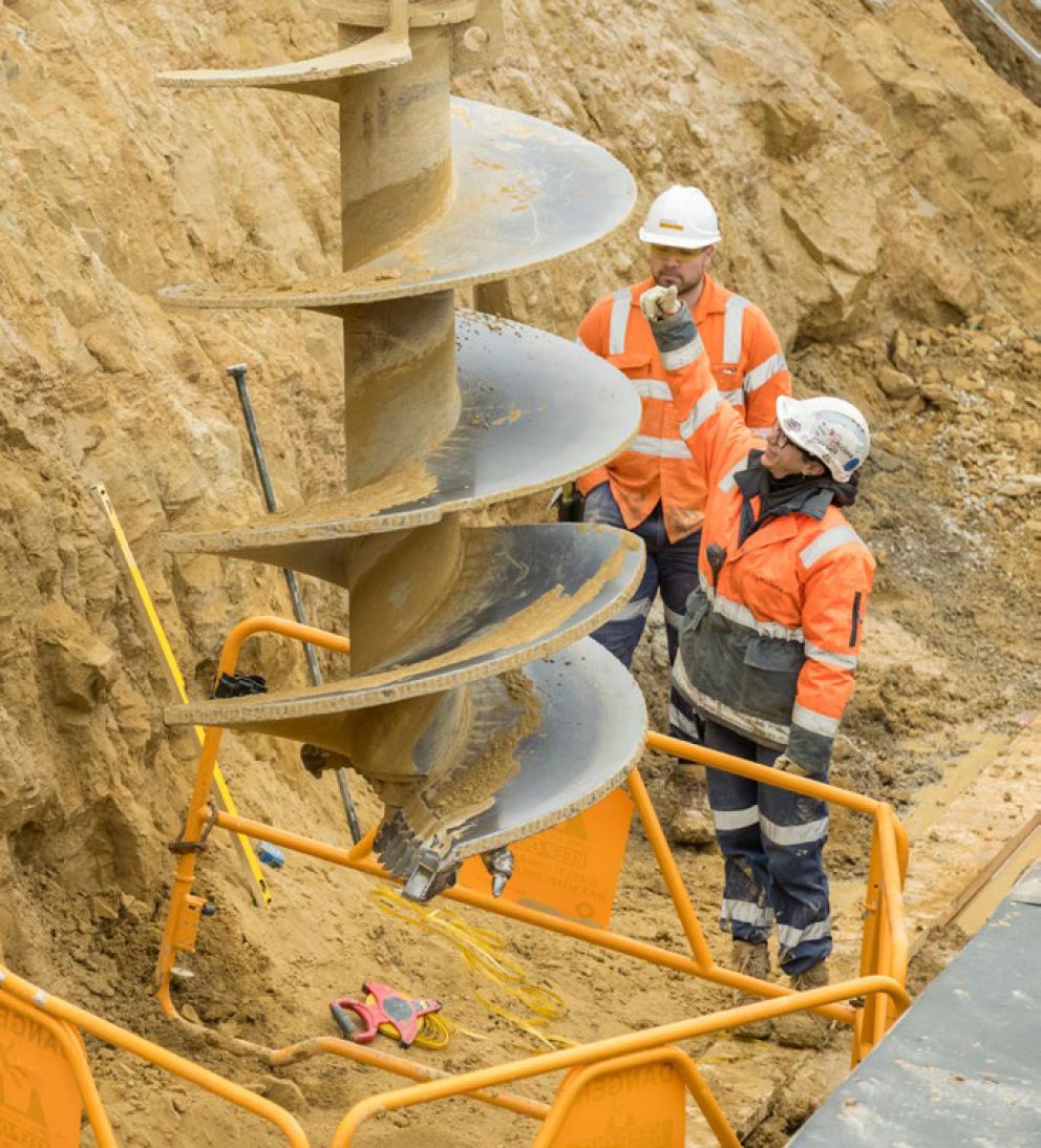 Workers inspecting a drill used for underground piling works