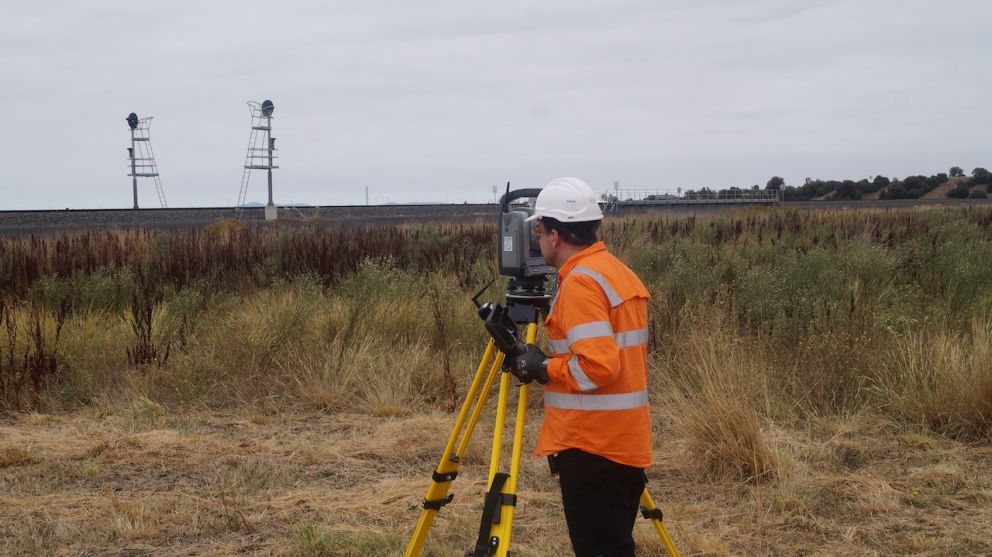 Worker in orange hi vis doing land surveying